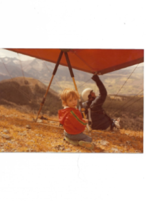 My son Zane siting under  a hang glider 1981.png